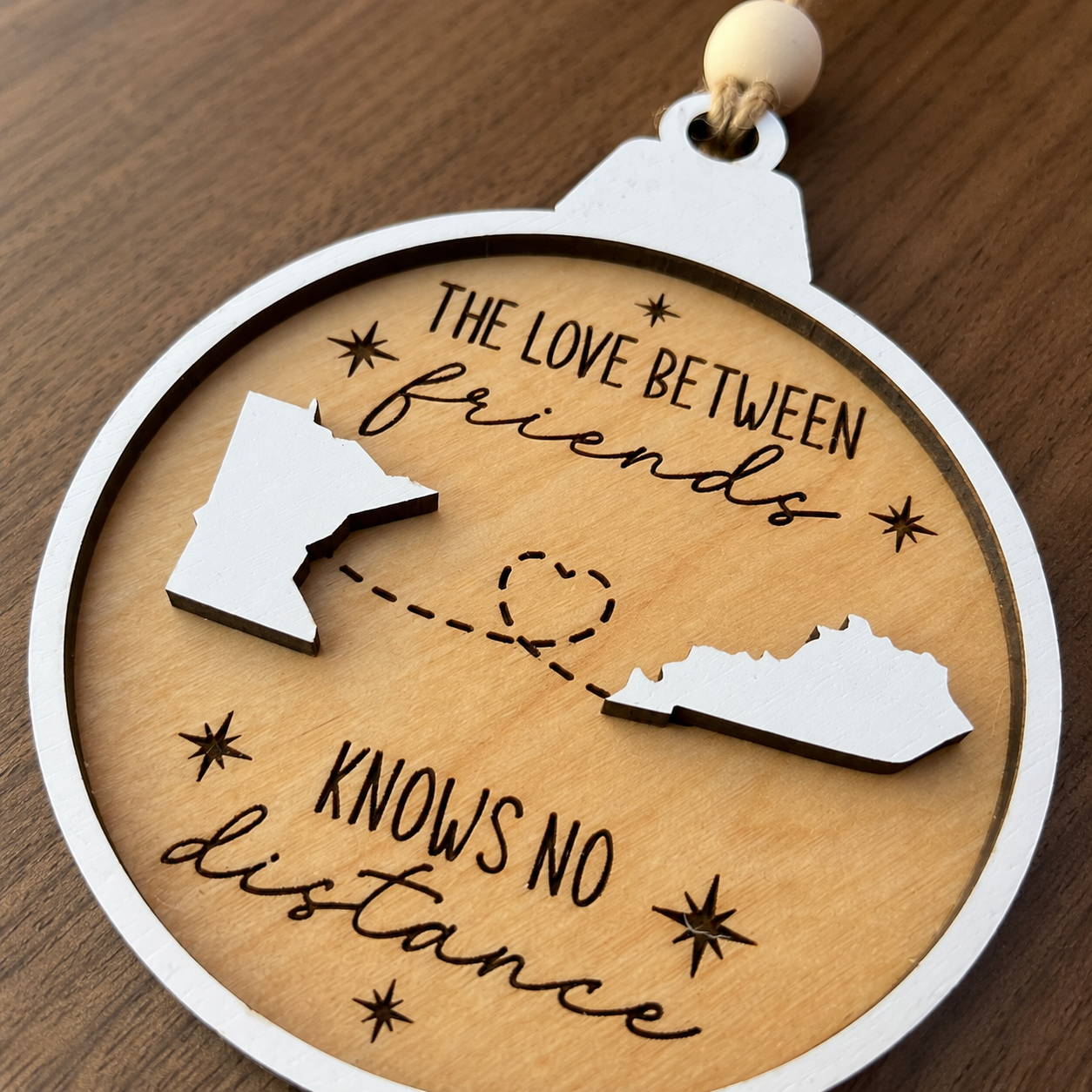 Close-up of a personalized long distance ornament showing engraved lettering, layered wood craftsmanship, and custom state cutouts.