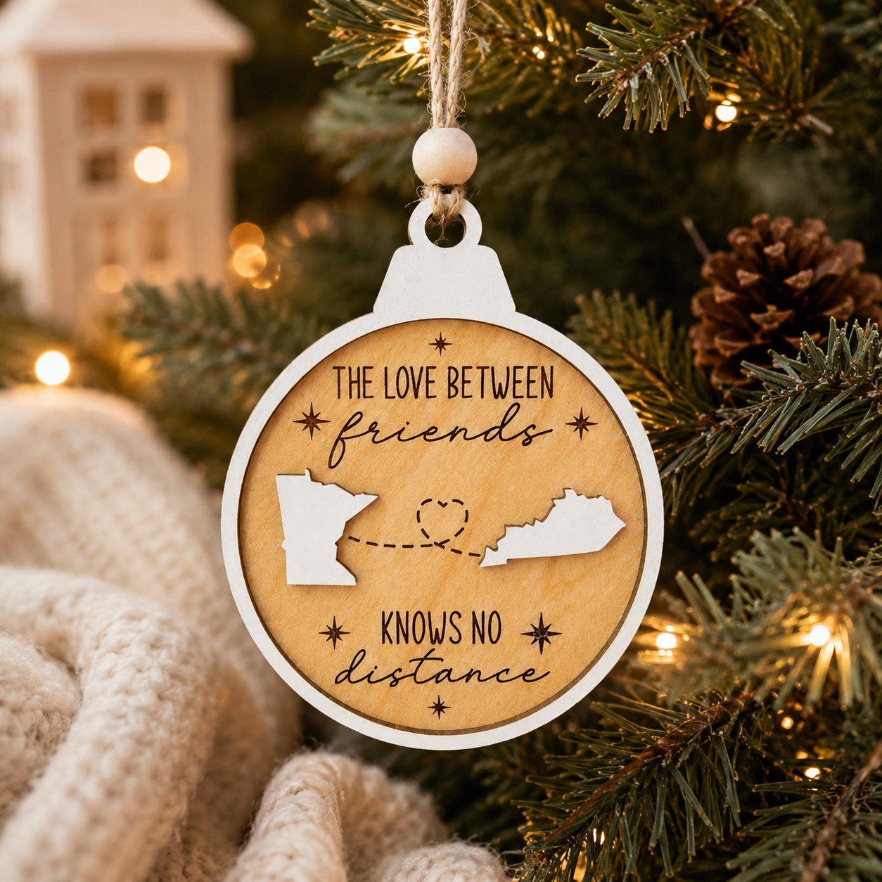 Handmade personalized long distance ornament hanging on a Christmas tree surrounded by warm holiday lights and festive décor.