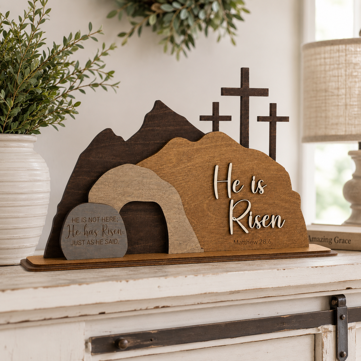 Handcrafted He Is Risen wooden Easter display styled on a rustic farmhouse console table with neutral home decor, greenery, and candle accents.
