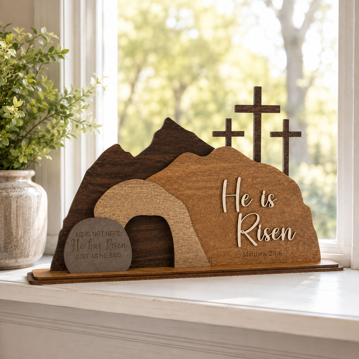 He Is Risen wooden resurrection scene displayed on a bright windowsill with natural sunlight, featuring the empty tomb, three crosses, and Matthew 28:6 scripture.