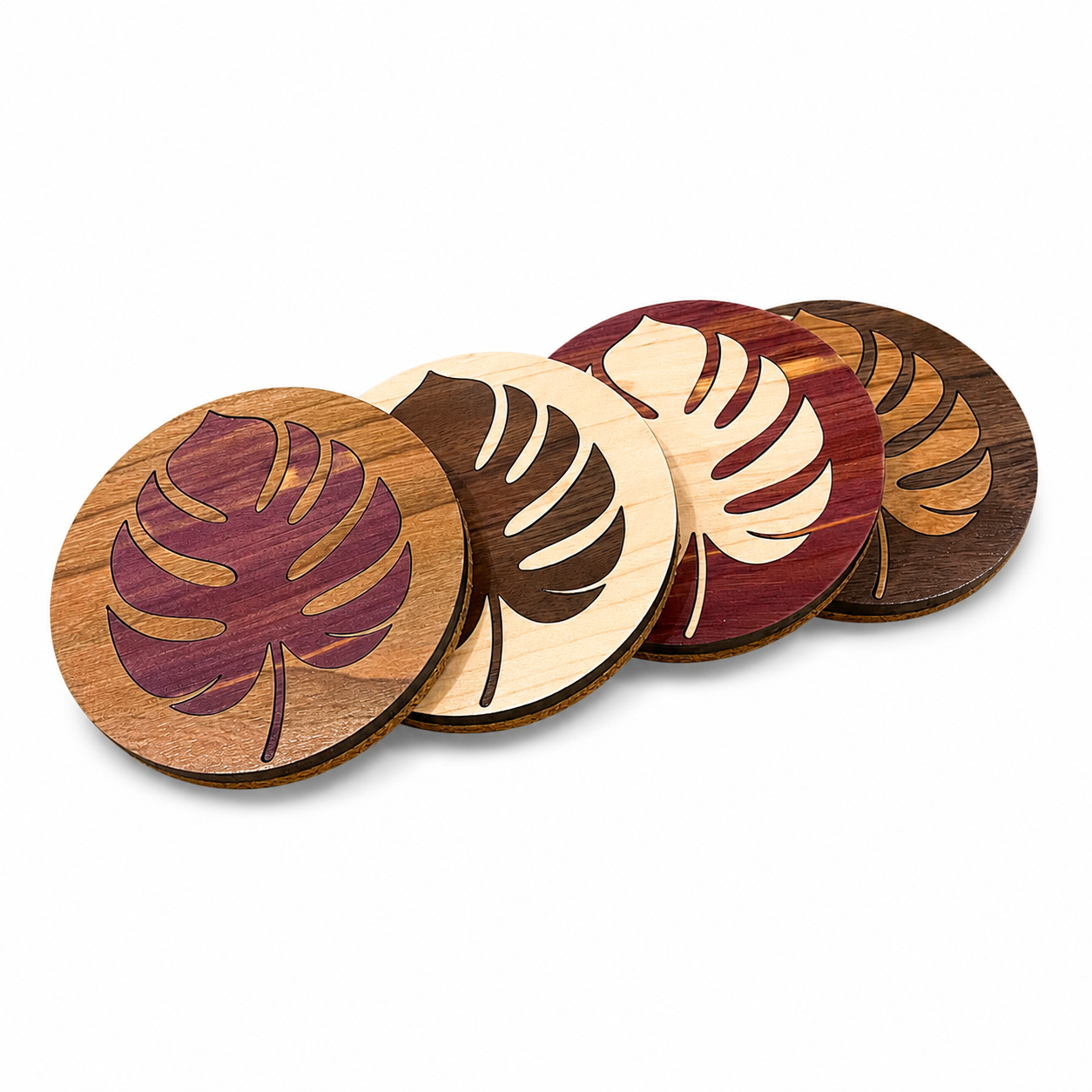 Four handcrafted hardwood Monstera coasters overlapping on a white background showing natural wood grain.
