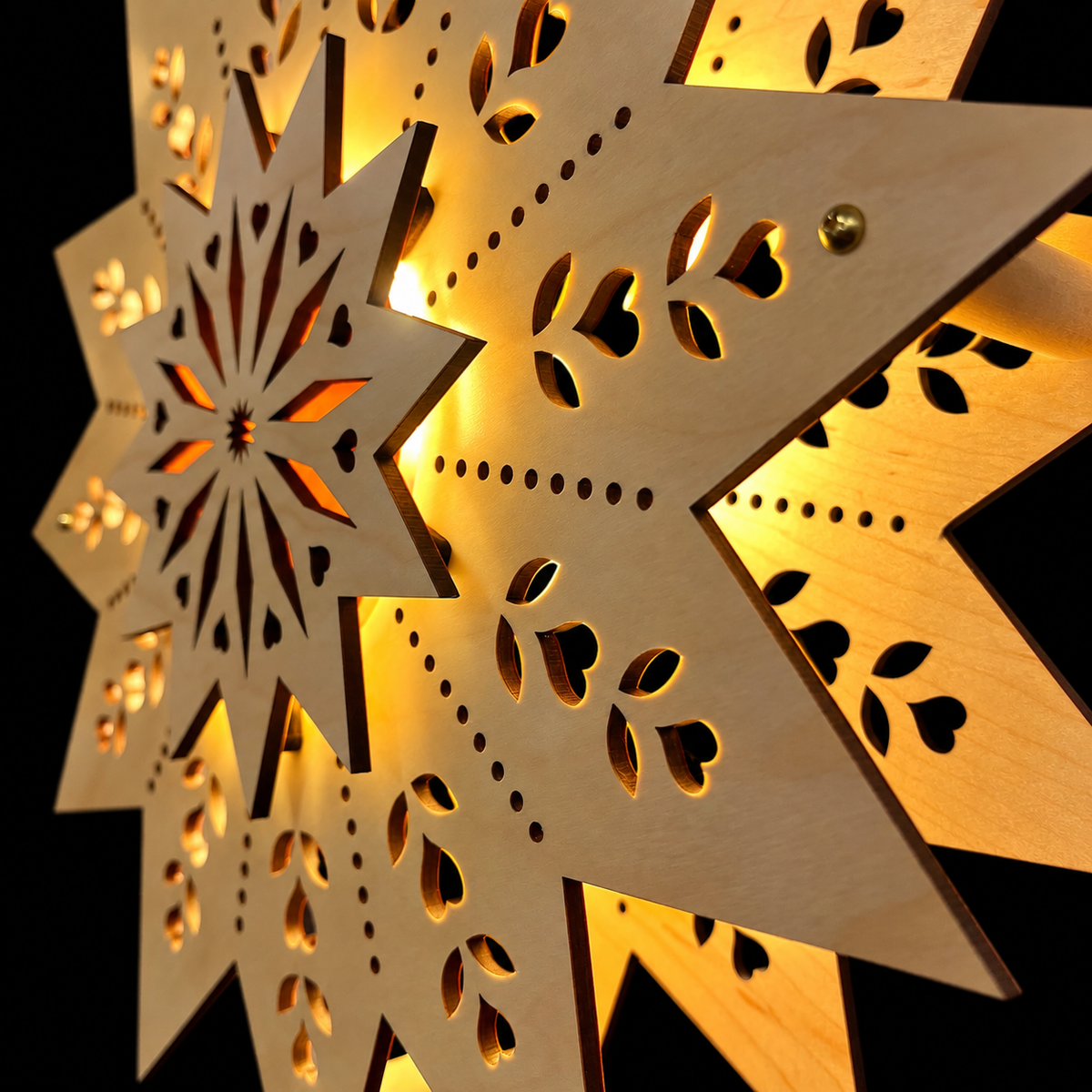 Close-up of the layered wooden Welcome Light showing delicate laser-cut hearts, leaves, natural wood grain, and warm light shining around the raised center star.